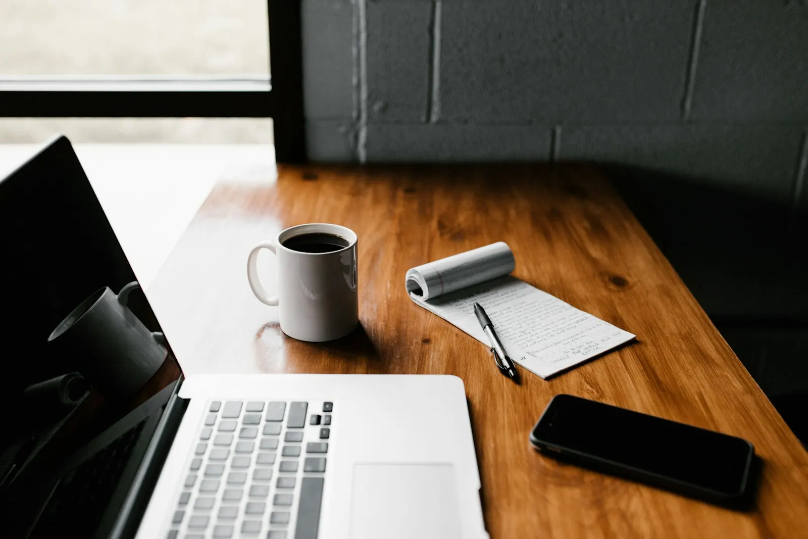 Portátil, taza de café y móvil sobre una mesa de trabajo preparada para planificar